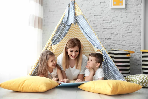 Nounou et petits enfants lisant le livre dans la tente à la maison — Photo