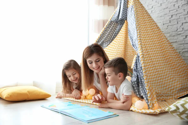 Chůva a malé děti čtení knihy ve stanu doma — Stock fotografie