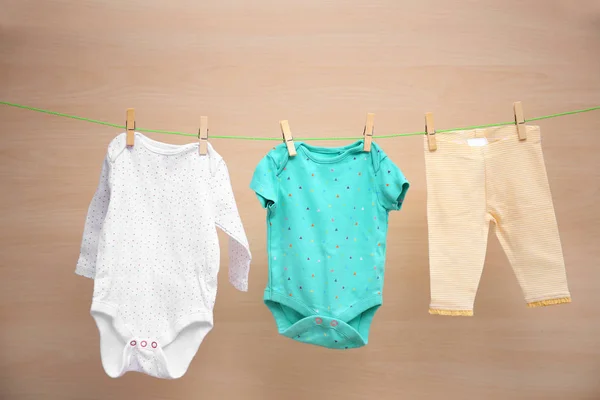 Babykleidung hängt an Wäscheleine vor Holzhintergrund — Stockfoto