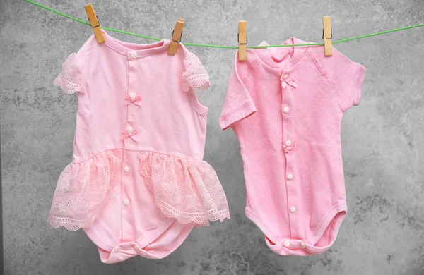 Roupas de bebê penduradas na linha de lavagem contra fundo cinza — Fotografia de Stock