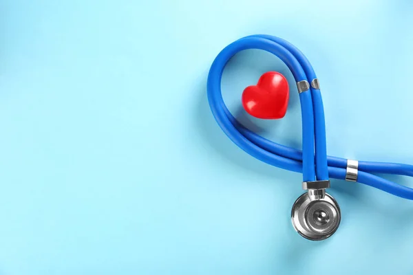 Estetoscopio y pequeño corazón rojo sobre fondo de color. Concepto de ataque cardíaco — Foto de Stock