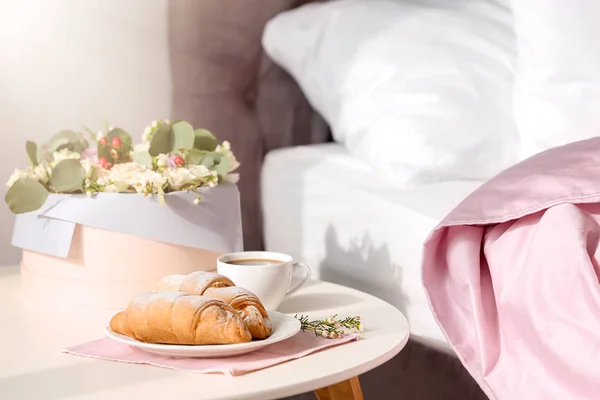 Тарелка с вкусными круассанами и чашкой кофе на столе возле кровати — стоковое фото