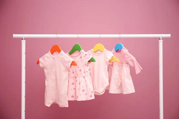 Babykläder hängande på rack mot färg bakgrunden — Stockfoto