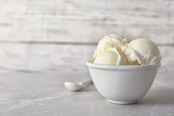 Tigela com saboroso sorvete de baunilha na mesa contra fundo leve — Fotografia de Stock
