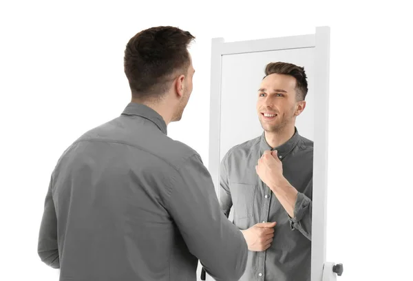 Young man looking at himself in mirror on white background — Stock Photo, Image