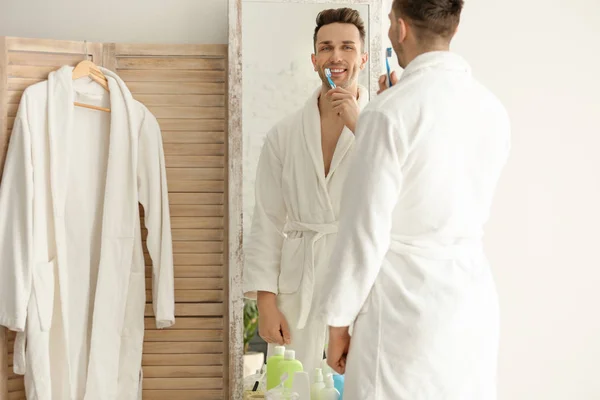 Молодий чоловік дивиться у дзеркало під час чищення зубів у приміщенні — стокове фото