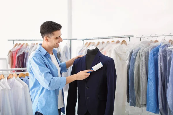 Anak muda mengeluarkan debu dari jaket dengan mesin penggulung di dry-cleaner 's — Stok Foto