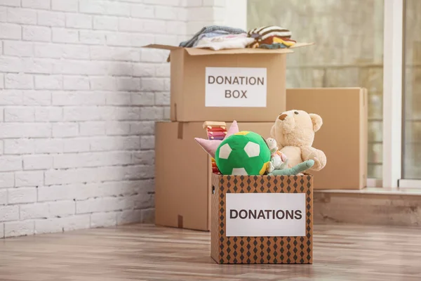 Caixas de doação com brinquedos e roupas no chão dentro de casa — Fotografia de Stock