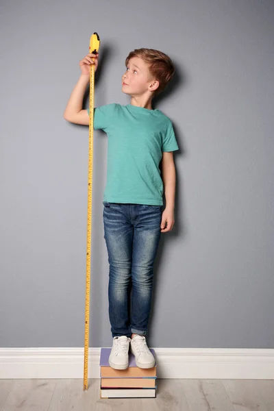 Маленький мальчик измеряет свой рост рядом с серой стеной — стоковое фото