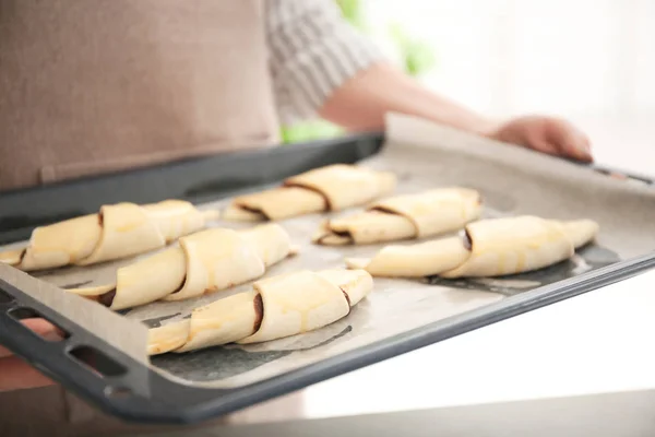 Vrouw met bakplaat met rauwe croissants binnenshuis — Stockfoto