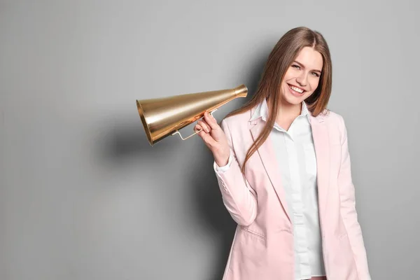 Jovem mulher com megafone em fundo cinza — Fotografia de Stock