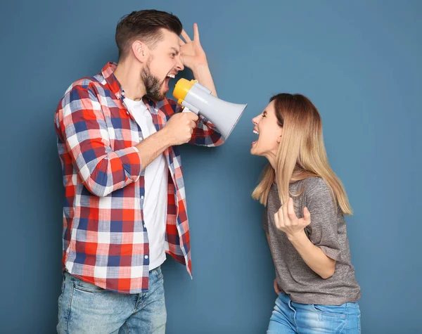 Jonge man met een megafoon schreeuwen op de vrouw op kleur achtergrond — Stockfoto