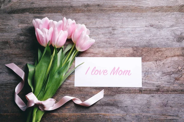 Komposition mit Grußkarte und Tulpen zum Muttertag auf Holzgrund, Draufsicht — Stockfoto