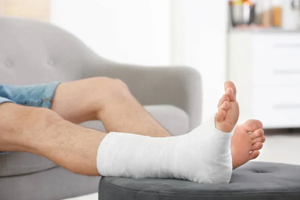 Junger Mann mit gebrochenem Bein sitzt zu Hause auf Sofa — Stockfoto