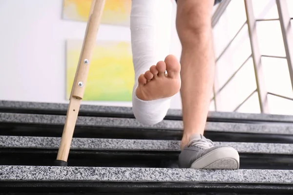 Joven con la muleta y la pierna rota en el yeso en las escaleras —  Fotos de Stock