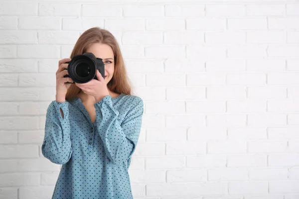 Женщина-фотограф с камерой на кирпичном фоне — стоковое фото