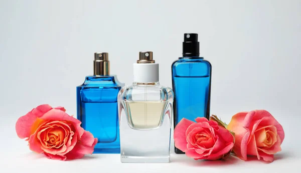 Kompozycja z przezroczystych butelek perfum i piękne kwiaty na białym tle — Zdjęcie stockowe