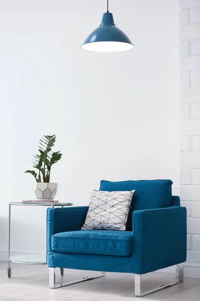 Современная лампа с растением на столе и кресле в помещении — стоковое фото