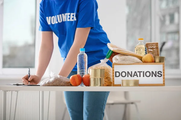 Mujer voluntaria listando productos alimenticios de la caja de donación en el interior — Foto de Stock