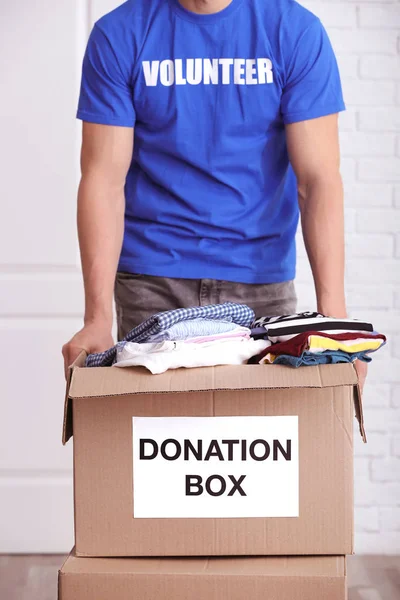 男性志愿者手持衣服在室内的捐赠箱 — 图库照片