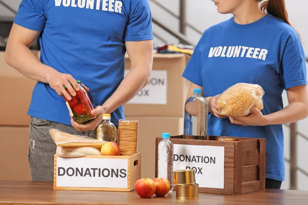 Voluntários colocando produtos alimentares em caixas de doação dentro de casa — Fotografia de Stock