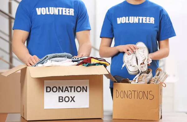 Voluntarios poniendo ropa y zapatos en cajas de donaciones en el interior — Foto de Stock