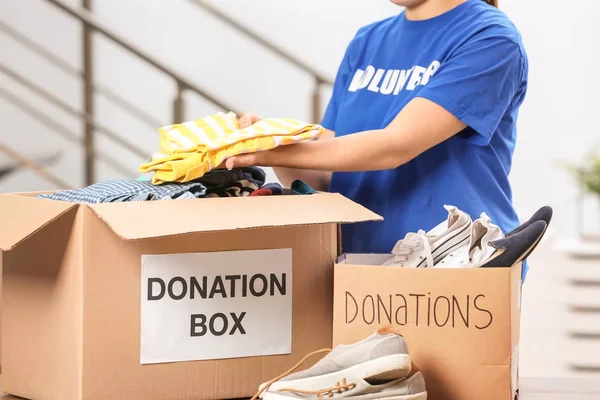Mujer voluntaria poniendo ropa en la caja de donaciones en el interior — Foto de Stock