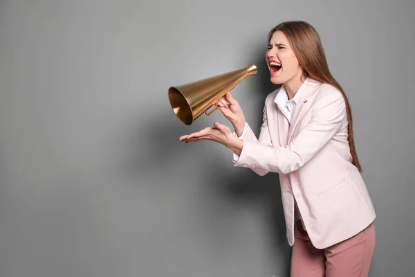 Jovem mulher gritando em megafone no fundo cinza — Fotografia de Stock