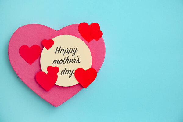 Surprise for Mother's Day with greeting card and paper hearts on color background