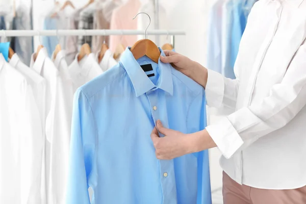 Jovem segurando cabide com camisa na lavandaria — Fotografia de Stock