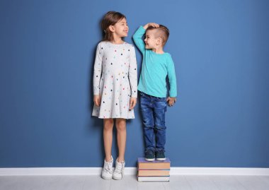 Little girl and boy measuring their height near color wall clipart