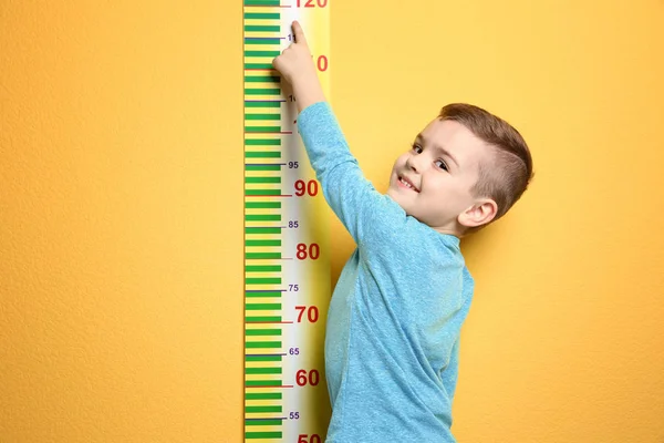 Kleiner Junge misst seine Körpergröße auf farbigem Hintergrund — Stockfoto