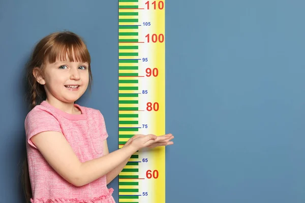 Little girl measuring her height on color background