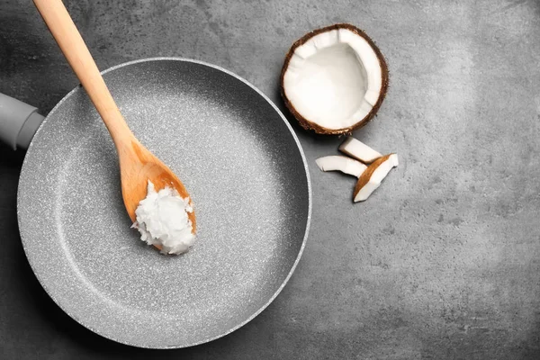 Sartén con aceite de coco y trozos de nuez sobre fondo gris — Foto de Stock