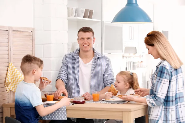 Los padres y los niños pequeños lindos desayunando con sabroso pan tostado en la mesa — Foto de Stock