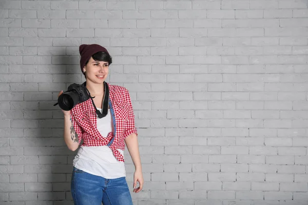 Young female photographer with camera on brick background — Stock Photo, Image