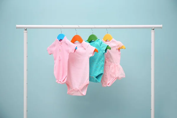 Baby clothes hanging on rack against color background — Stock Photo, Image