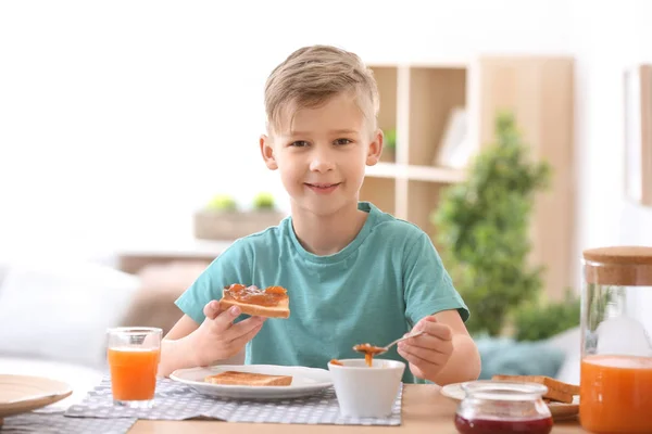 Cute little boy spreading jam onto tasty toasted bread at table