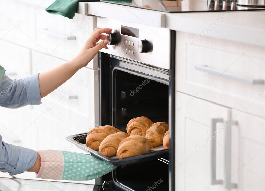 Woman taking baking tray with croissants out of oven in kitchen