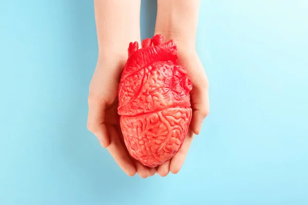 Mujer sosteniendo modelo de corazón sobre fondo de color. Concepto de ataque cardíaco — Foto de Stock