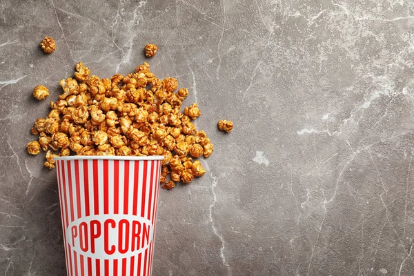 Köstliches Popcorn mit Karamell in Papiereimer auf grauem Hintergrund, Draufsicht — Stockfoto