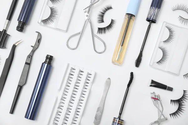 Composição de leigos planos com pestanas falsas e ferramentas cosméticas no fundo branco — Fotografia de Stock