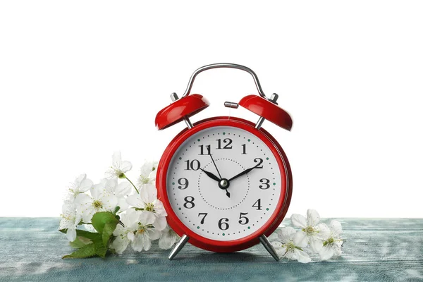 Reloj despertador y rama con flores de primavera sobre mesa de madera sobre fondo blanco. Concepto de cambio de tiempo — Foto de Stock