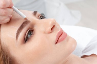 Cosmetologist preparing young woman for  eyebrow permanent makeup procedure, closeup clipart