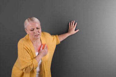 Mature woman having heart attack on color background clipart