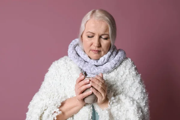 Mature woman with cup of hot tea suffering from cold on color background — Stock Photo, Image