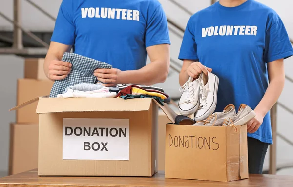 Voluntarios poniendo ropa y zapatos en cajas de donaciones en el interior — Foto de Stock