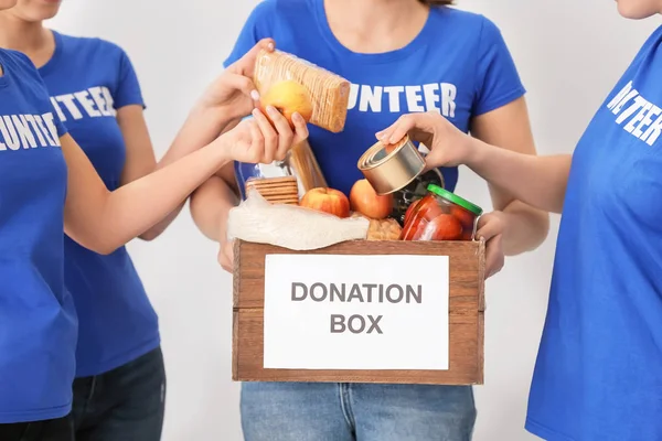 Добровольцы кладут продукты питания в коробку для пожертвований на светлом фоне — стоковое фото
