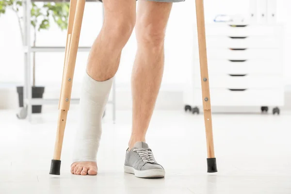 松葉杖、屋内で上に立っているキャストに足の骨折を持つ男 — ストック写真