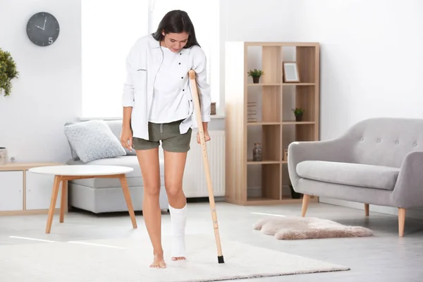 Mujer joven con muleta y pierna rota en yeso en casa —  Fotos de Stock